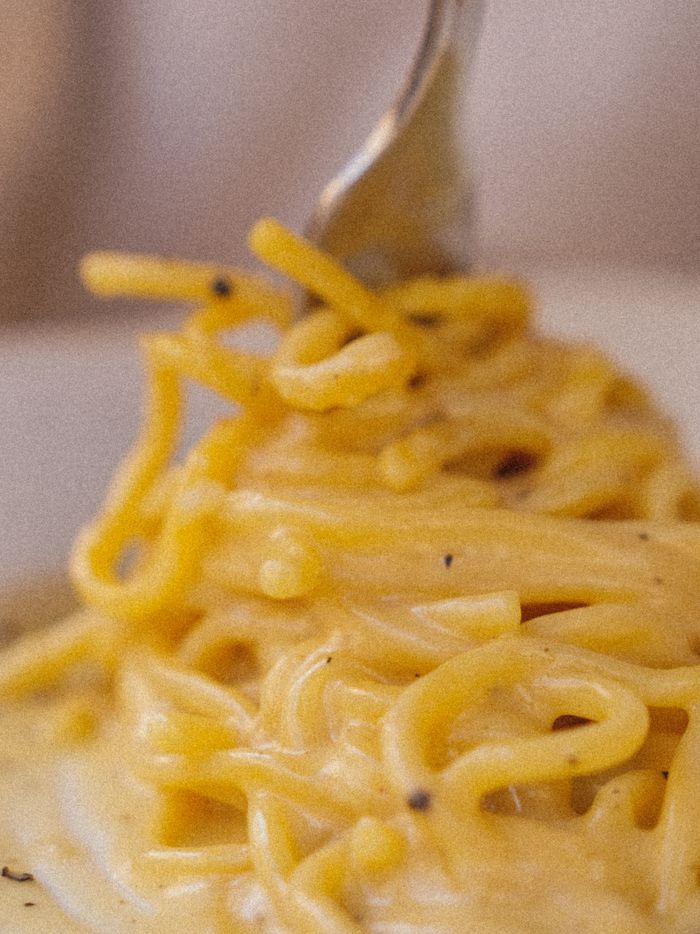 Close-up of a fork twirling creamy carbonara pasta, capturing rich texture and savory flavors.
